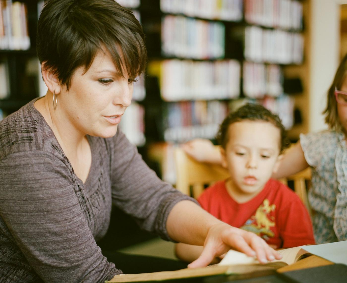 A guide sits beside a young boy, showing him a book
