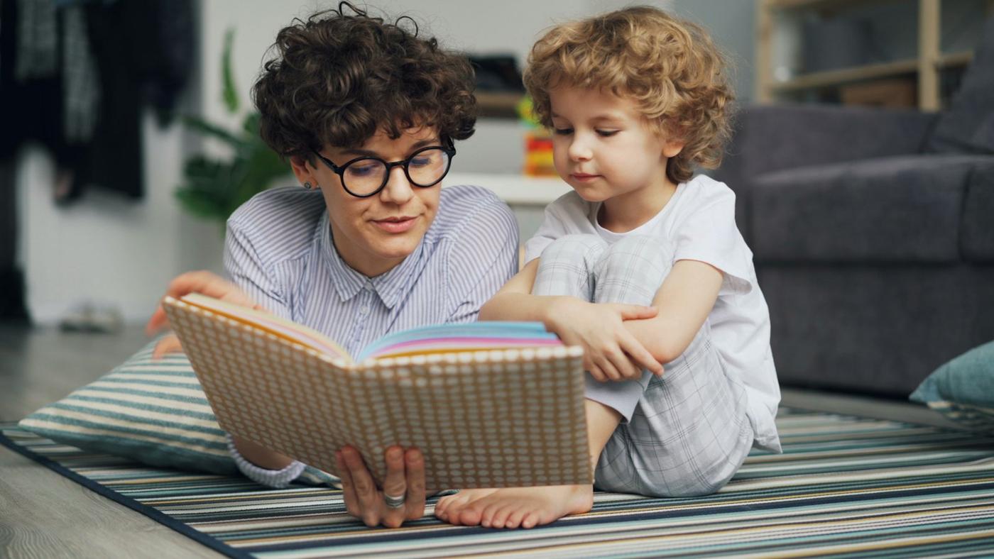 An adult and child read a book together on the floor