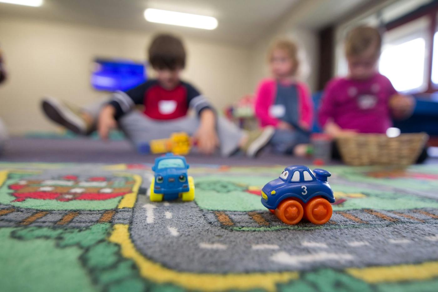 Children work with toy cars on a classroom rug